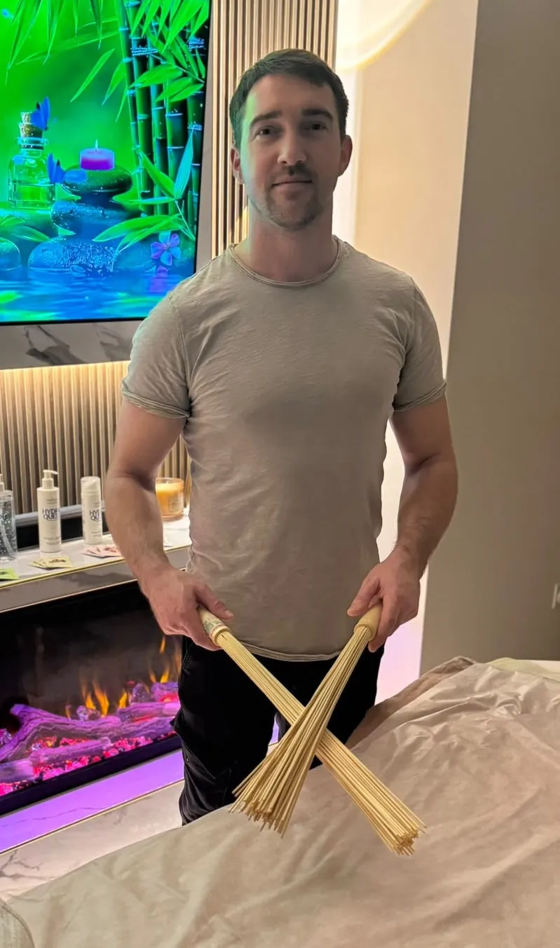 Constantin standing beside a massage table, holding bamboo massage sticks